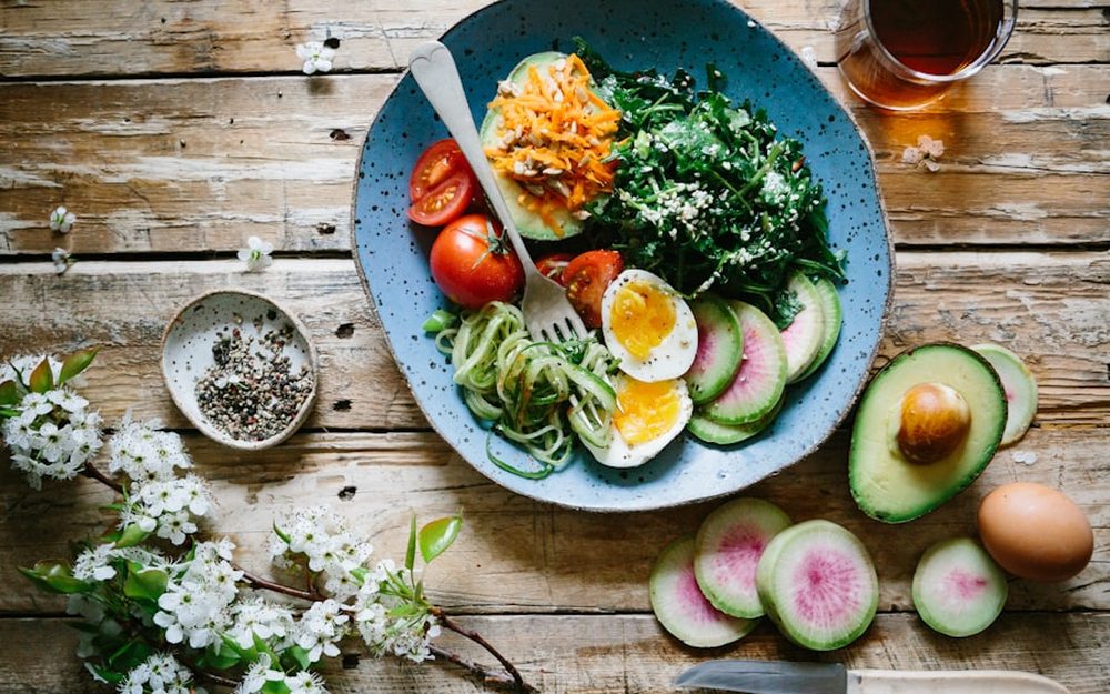 Prato equilibrado com folhas verdes, ovo, abacate e vegetais coloridos